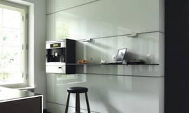 De multifunctionele wand van deze keuken is uit blokken opgebouwd. De apparatuurkast heeft exact de hoogte van één blok. Links ziet u een keukeneiland met metalen wangen en aanrechtblad en donkere houten fronten. Zuordnung: Stil Design-keukens, Planungsart Detail keukenontwerp